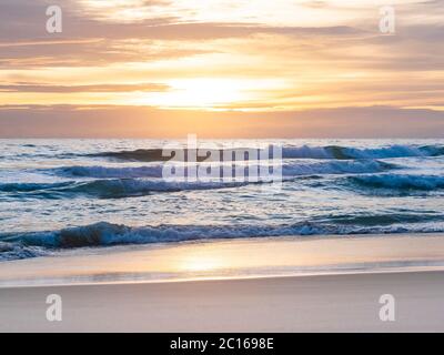 Sand mit Meereswelle traf den Strand, wolkiger Himmel bei Sonnenuntergang Stockfoto