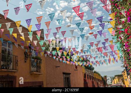 Papierfesta Banner genannt Papel picado vor einem blauen Himmel und klassischen Kolonialgebäude entlang der Calle Quebrada im historischen Viertel von San Miguel de Allende, Mexiko. Stockfoto