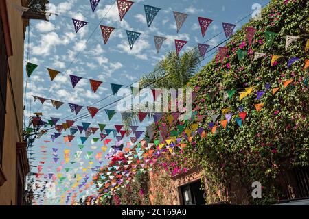 Papierfesta Banner genannt Papel picado vor einem blauen Himmel und klassischen Kolonialgebäude entlang der Calle Quebrada im historischen Viertel von San Miguel de Allende, Mexiko. Stockfoto