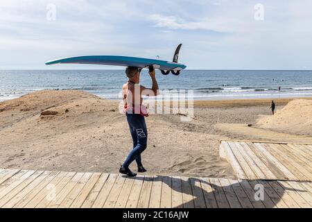 Die Anwohner haben den Strand für sich, da das Wetter für den Sommer hochgeht. Surfer trägt sein Board auf dem Kopf ans Ufer. Phase 3 De-Escalati Stockfoto