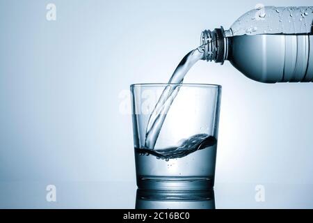 Wasser in einen Becher in Nahaufnahme auf den Flaschenhals gießen und Flüssigkeit mit Spritzer über Grau mit Copyspace Stockfoto