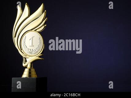 Gewinner Goldtrophäe mit gravierter Medaillon mit Nummer 1 und Lorbeerkranz umgeben von einem Wirbel über einem dunkelblauen Hintergrund mit Copyspace für einen cha Stockfoto