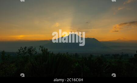 Blick auf einen Sonnenaufgang mit der dunklen Silhouette des Vulkans Imbabura, wobei die Sonne hinter dem Berg aufgeht und den klaren Himmel mit gelbem Licht erhellt Stockfoto