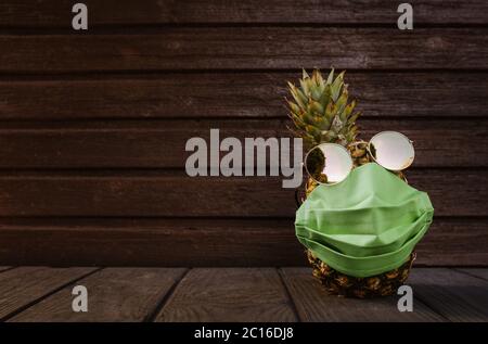 Kühle Ananas mit Sonnenbrille und Gesichtsmaske auf dunklem Holzhintergrund. Hochwertige Fotos Stockfoto