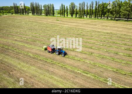 Ein Traktor mit einem gezogenen Ballen Maschine machen sammelt Strohrollen auf dem Feld und macht die Runde großen Ballen Stockfoto