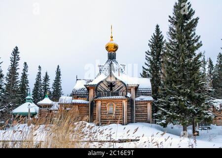 Alte Holzkirche mit goldener Kuppel und Kreuz, Häuser im Dorf im Winter Stockfoto