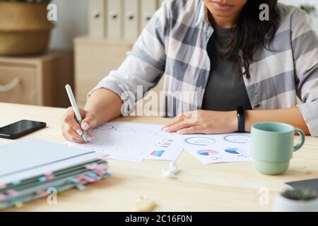 Beschnittenes Porträt einer jungen Frau mit gemischter Rasse, die Grafiken und Diagramme zeichnet, während sie zu Hause ein Projekt plant, Raum kopieren Stockfoto