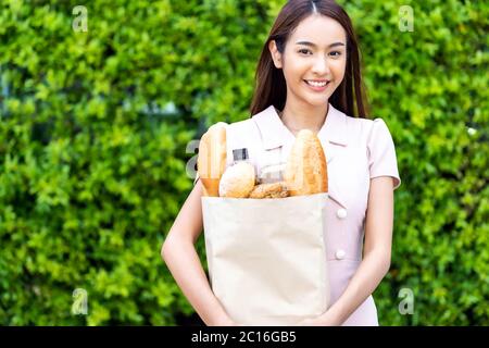 Portrait von attraktiven und lächeln asiatische Frau hält Lebensmitteltasche kaufen aus Supermarkt. Essen und Trinken und Konsumdenken Kaufkonzept. Stockfoto