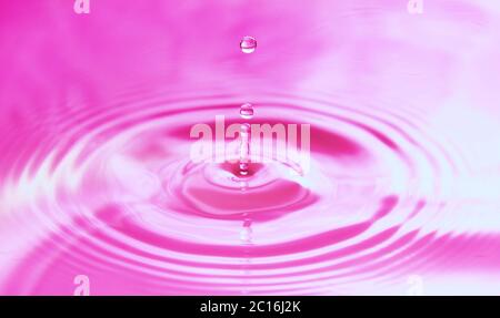 Wassertropfen fallen ins Wasser und bilden perfekte konzentrische Kreise. Abstrakter rosa Hintergrund. Stockfoto