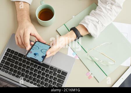 Draufsicht Nahaufnahme eines nicht erkennbaren Mannes, der Smartphone benutzt, während er im Home Office in minimaler Lichteinstellung arbeitet, Kopierfläche Stockfoto