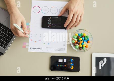 Draufsicht Nahaufnahme eines nicht erkennbaren Mannes, der Smartphone benutzt, während er im Home Office geschäftlich arbeitet, minimales Hintergrundbild, Kopierplatz Stockfoto