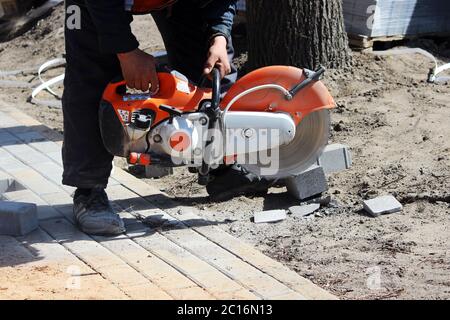 Ein Maurer arbeiten schneidet die Bürgersteig Kachel mit einer Kreissäge während der Reparatur der Bürgersteig in der Stadt. Stockfoto