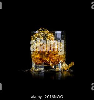 Glas spritzendem Whiskey oder anderen Alkohol mit Eiswürfel isoliert auf schwarzem Hintergrund Stockfoto