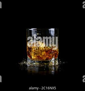 Glas spritzendem Whiskey oder anderen Alkohol mit Eiswürfel isoliert auf schwarzem Hintergrund Stockfoto