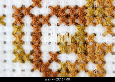 Makro Schuss Fragment Stickerei Muster braun Faden handgemachte Stickerei, Muster im Kreuzstich-Stil auf weißem Stoff Stockfoto