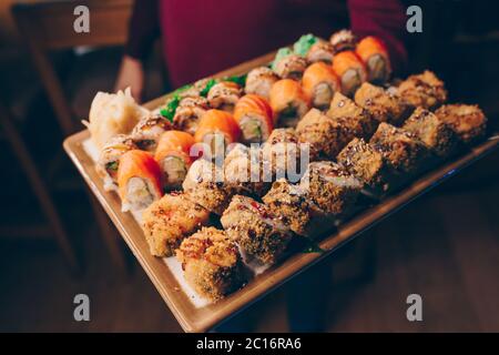 Close-up Hand Kellner Holding Set köstliche frische Sushi Schieferteller, japanische rohe Fisch warm Ebi Sake Unagi . Philadelphia Flesh Rolls serviert auf Teller i Stockfoto