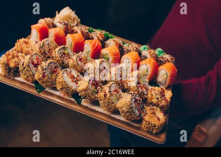 Close-up Hand Kellner Holding Set köstliche frische Sushi Schieferteller, japanische rohe Fisch warm Ebi Sake Unagi . Philadelphia Flesh Rolls serviert auf Teller i Stockfoto