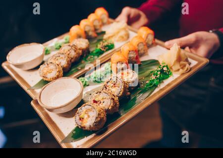 Close-up Hand Kellner Holding Set köstliche frische Sushi Schieferteller, japanische rohe Fisch warm Ebi Sake Unagi . Philadelphia Flesh Rolls serviert auf Teller i Stockfoto