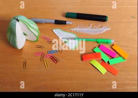 Bürobedarf auf alten, zerkratzten Schreibtischplatte. Weiße Feder, grüner Stift, schwarzer und grüner Marker und grauer Stift. Büroklammern und bunte Post it Tabs lyi Stockfoto