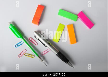 Bunte Stifte, Büroklammern und Post-it-Tabs verteilen sich auf einem Stück weißem Papier. Von oben aufgenommen. Stockfoto