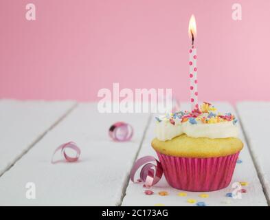 Ein Cupcake mit brennender Kerze auf weißem Tisch vor rosa Hintergrund - selektiver Fokus Stockfoto