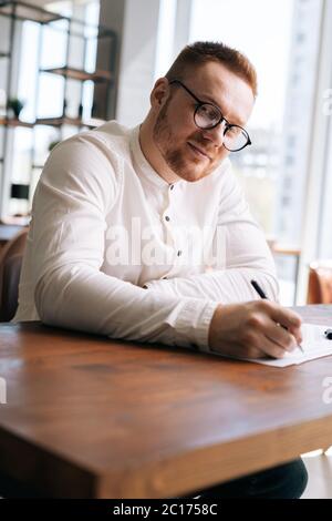 Geschickter junger Songwriter mit stilvollen Brillen schreibt mit Stift Note des Liedes Stockfoto