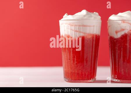 Erdbeer Smoothie Shakes im Glas mit Schlagsahne auf rotem Hintergrund mit Copy Space.Summer erfrischenden Drink Mocktail close-up Stockfoto