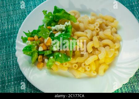 Pasta mit Garnierung: Salat, Ketchup, Mais, Rührei mit Knistern auf blauer Serviette. Portion Pasta auf einem weißen Teller Stockfoto
