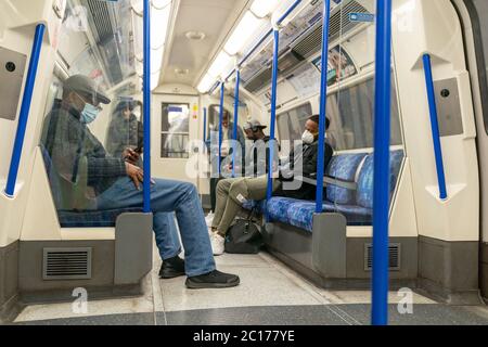 LONDON, ENGLAND - 8. JUNI 2020: Gruppe von Männern auf einer Piccadilly Line London Underground Train Carriage mit Gesichtsmasken während COVID-19 Coronavirus 3 Stockfoto