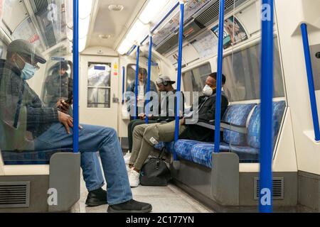 LONDON, ENGLAND - 8. JUNI 2020: Gruppe von Männern auf einer Piccadilly Line London Underground Train Carriage mit Gesichtsmasken während COVID-19 Coronavirus 2 Stockfoto