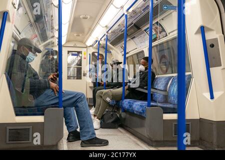 LONDON, ENGLAND - 8. JUNI 2020: Gruppe von Männern auf einer Piccadilly Line London Underground Train Carriage mit Gesichtsmasken während COVID-19 Coronavirus 1 Stockfoto