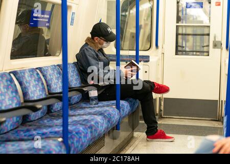 LONDON, ENGLAND - 8. JUNI 2020: Junger Mann auf einer Piccadilly Line London Underground Train Carriage mit Gesichtsmaske während COVID-19 Coronavirus 1 Stockfoto