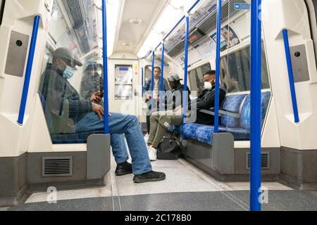 LONDON, ENGLAND - 8. JUNI 2020: Gruppe von Männern auf einer Piccadilly Line London Underground Train Carriage mit Gesichtsmasken während der COVID-19 Pandemie 4 Stockfoto