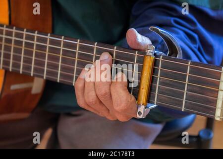 Annäherung an die linke Hand eines älteren Mannes, der eine Gitarre spielt, gekleidet in einem blauen Hemd Stockfoto
