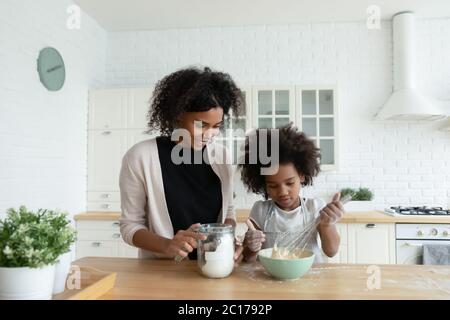 Kleine afrikanische Tochter und Mutter kochen zusammen Kuchen in der Küche Stockfoto