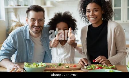 Fröhliches multiethnisches Paar mit Tochter, die in der Küche zusammen kocht Stockfoto