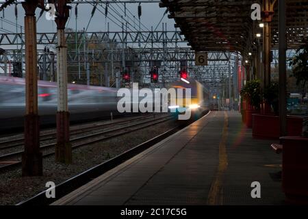 Vorbeifahrende Züge mit Bewegungsunschärfe und roten Signalen an der Hauptlinie der Westküste am Bahnhof Crewe. Stockfoto