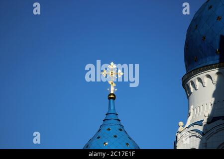 Das vergoldete Kreuz leuchtet auf der Kuppel der Kirche Kathedrale der Heiligen Jungfrau auf einem blauen Himmel Hintergrund in der Stadt Gatchina, Stockfoto