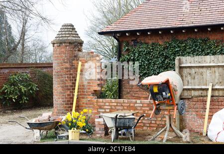 Bauarbeiten mit Werkzeugen und Zementmischer, Bau einer Ziegelgartenwand außerhalb eines britischen Hauses Stockfoto