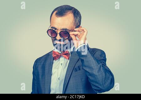 Skeptisch reifen, mittleren Alters Mann hält Sonnenbrille nach unten Blick auf Sie, Kamera zweifelhaft isoliert auf grün gelb einheitlichen Gradienten Hintergrund. Positi Stockfoto