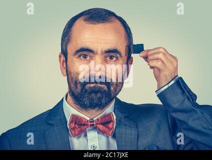 Konzept für externen Speicher erforderlich. Portrait von unglücklichen bärtigen Geschäftsmann trägt elegante Jacke und rote Fliege hält Micro SD-Karte in der Nähe seines Kopfes iso Stockfoto