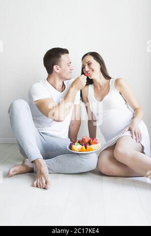 Junger Mann und schwangere Frau mit Obstteller drinnen Stockfoto