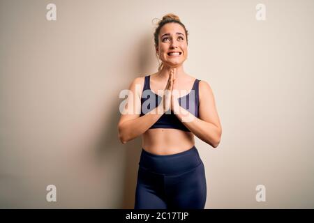Junge schöne blonde Sportlerin Sport treiben tragen Sportkleidung über weißem Hintergrund betteln und beten mit Händen zusammen mit Hoffnung Ausdruck o Stockfoto