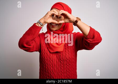 Mittlere Alter Brünette Frau trägt muslimische traditionelle Hijab über isoliert weißen Hintergrund tun Herzform mit Hand und Finger lächelnd suchen thro Stockfoto