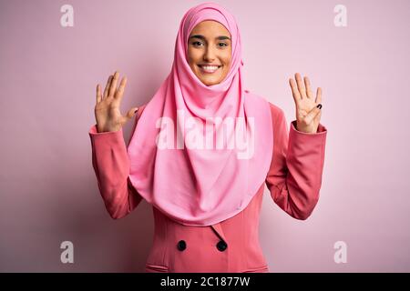 Junge schöne Brünette Geschäftsfrau trägt rosa muslim Hijab und Business Jacke zeigen und zeigen mit den Fingern Nummer neun, während lächelnd Co Stockfoto