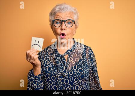 Ältere schöne grauhaarige Frau hält Erinnerungspapier mit traurigen Emotionen Gesicht Angst im Schock mit einem Überraschungsgesicht, Angst und aufgeregt vor Angst exp Stockfoto