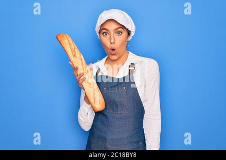 Junge schöne blonde Bäckerin Frau mit blauen Augen hält Laib hausgemachtes frisches Brot Angst im Schock mit einer Überraschung Gesicht, Angst und aufgeregt mit f Stockfoto