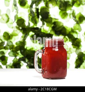 Erdbeer Smoothie oder Milchshake in einem Glas auf grünem Blatthintergrund. Stockfoto