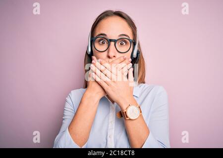 Junge schöne Call Center-Agent Frau trägt Brille mit Headset arbeiten schockiert, den Mund mit Händen aus Versehen. Geheimkonzept. Stockfoto