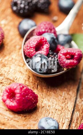 Reife und süße Beeren in einem Löffel auf Holzgrund Stockfoto